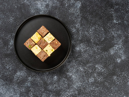 Indian sweets lying on a black plate on a black background. Assorted Indian sweets: Coconut Soan...