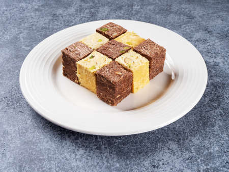 Indian sweets lying on a white plate on a gray background. Assorted Indian sweets: Coconut Soan Papdi, Chocolate Soan Papdi, Premium Soan Papdi, Mango Soan Papdi. side view.の写真素材