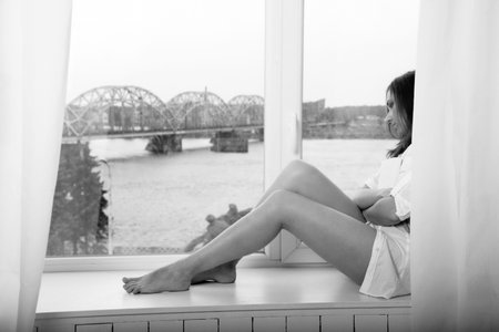 thoughtful woman with a book sitting near windowの写真素材