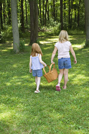Two young girls carrying a picnic basket in a shady park.の写真素材