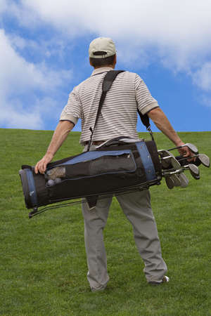 Man walking up hill carry bag of golf clubs.の写真素材