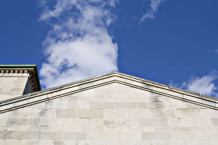 The roofline of a stone building againts a very blue sky with wisps of white clouds.の写真素材