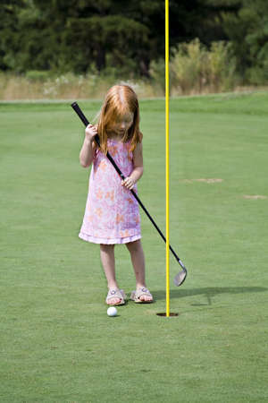 Small red-haired girl trying to get the golf ball into the hole.の写真素材