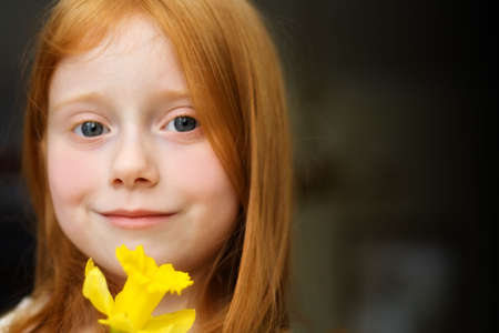 A very young red haired girl holding a yellow daffodil の写真素材