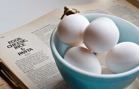 Old bowl of eggs sitting on top of an old recipe book - eggs, cheese, rice, pasta chapter.の写真素材