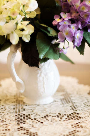 Pitcher of hydrangea with doily on table.  Soft focusの写真素材