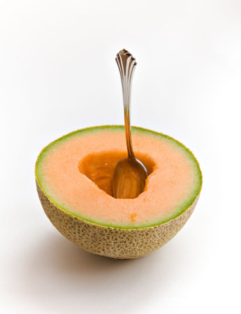 A spoon in a half of cantaloupe on white background.