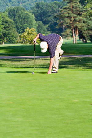 A male golfer bends to retrieve his ball from the hole. Space for copy in foreground. の写真素材