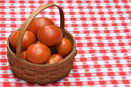A wooden woven basket of fresh garden tomatoes on tablecloth.の写真素材