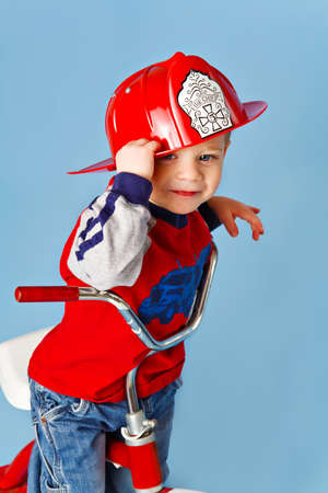 A two year old toddler wearing a fireman's helmet plays fireman on his tricycle.の写真素材