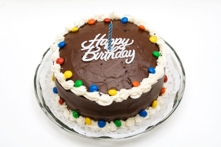 A chocolate birthday cake with candy, candle and icing.