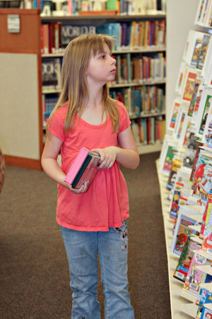 A elementary school-age child browsing library shelves for materials to borrow. 