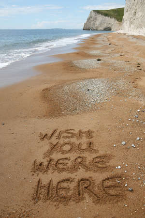 'Wish you were here' written in the sand on a peaceful beach - good copy areaの写真素材
