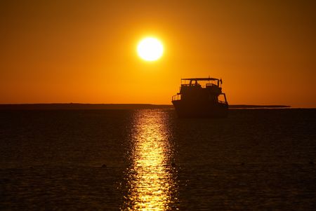 Boat silhouette and golden sunrise over the oceanの写真素材