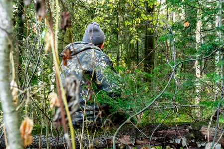 In the woods a man in camouflage sits on a logの写真素材