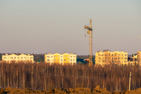 mid-rise houses built and tower crane are located behind a birch forest, in distance you can see the...