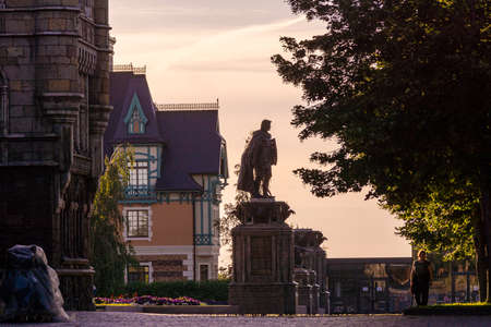 Khryashchevka, Russia, July 16, 2020, Garibaldi castle, against background of evening sky, statue of warrior in front of stone castle, in the distance half-timbered house, woman is walking along pathのeditorial素材