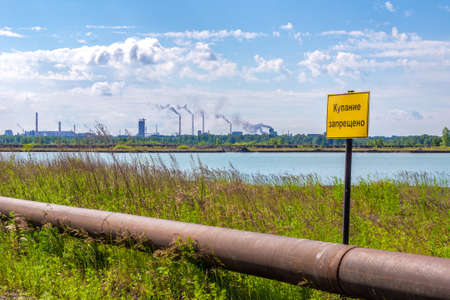 warning sign - swimming is prohibited near the slurry pipeline to the dump for settling, there are many chimneys of factories in the distanceの写真素材
