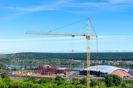 yellow tower crane on the background of the river, on the bank of which the construction of...
