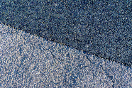 Old and cracked from climatic influences gray asphalt merges with new black asphalt