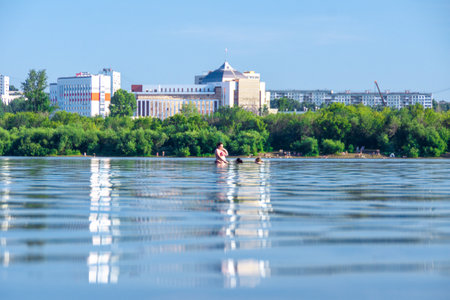against the backdrop of high-rise buildings of a coastal city illuminated by the summer sun, a plump woman stands waist-deep in water, her friends swim up to her, selective focusの写真素材