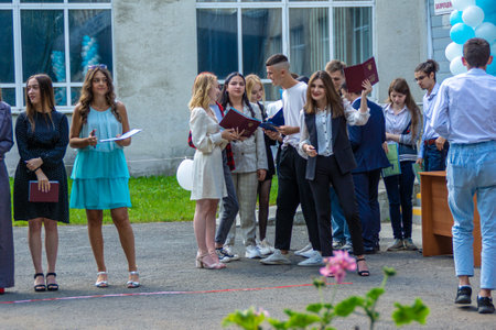 Russia, Kemerovo - 07, 2021. Outdoors, graduates of an educational institution receive a document of graduation, a young woman rejoices at receiving a university diploma, selective focusのeditorial素材