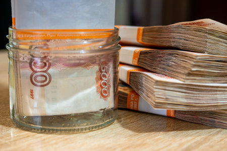 5000 Russian ruble bills in packs in a small glass jar and on a table nearby, close-up and selective...