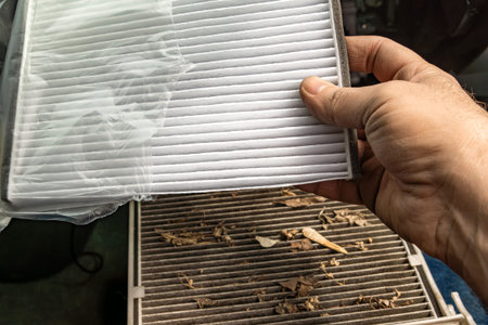 A person taking a clean new cabin air filter out of its plastic packaging, holding it over a very...