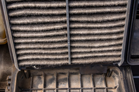 A person removing a very dirty engine air filter from the car's intake system, showing how much dust it has collected and why regular changes are important with selective focus on the filter surfaceの写真素材