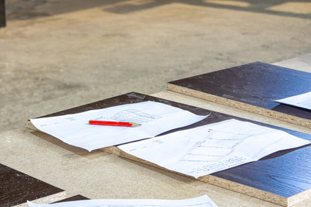 Wood panels and paper plans with a red pencil lie on a worktable, showing how workers check pieces...
