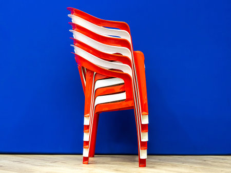 Photo of stacked red and white plastic chairs from the side with shiny surfaces against blue background showing practical chair storage, selective focusの写真素材