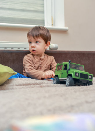 Little boy sitting on the bed among the toys at homeの写真素材