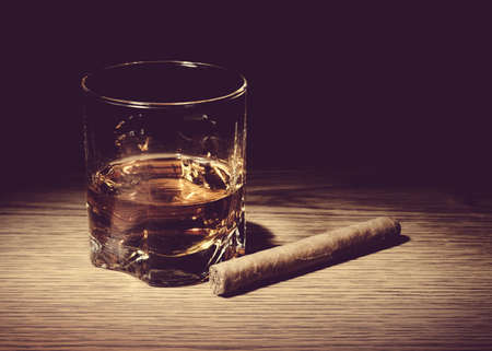 Vintage style image of glass of whiskey and a cigar on wooden tableの写真素材