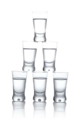 Close-up view of many glasses of vodka standing on each other isolated on whiteの写真素材
