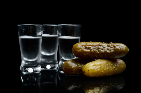 Studio shot of glasses of vodka with pickled cucumbers isolated on black backgroundの写真素材