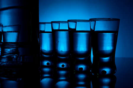 Studio shot of bottle with many glasses of vodka lit with blue backlightの写真素材