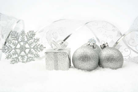 Decoration of silver christmas baubles and gifts with ribbon on snow on white backgroundの写真素材