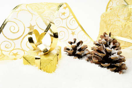 Decoration of golden christmas gifts with ribbon and pine cones on snowの写真素材