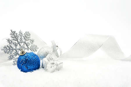 Decoration of silver and blue glitter baubles with ribbon and snowflake on snow on white backgroundの写真素材