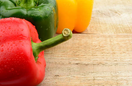 Closeup view of three coloured peppers on wooden bright plank, boardの写真素材