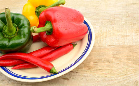 Closeup various peppers on wooden rural kitchen table on plateの写真素材