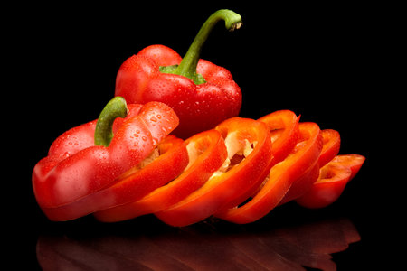 Studio shot of slices of red bell peppers isolated on black background with drops of water