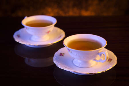 Old-style image with two porcelain cups of tea on black backgroundの写真素材