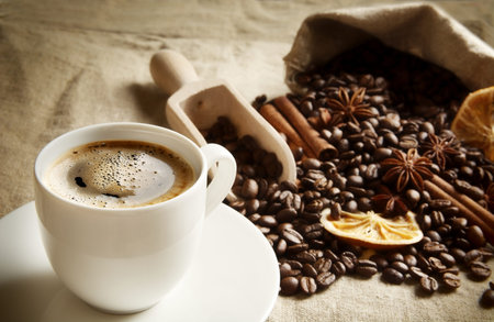 Overturned sack full of coffee beans with coffee cup, dried oranges,anises and cinnamon on linen