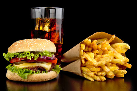Big single cheeseburger with glass of cola and french fries on black wooden desk