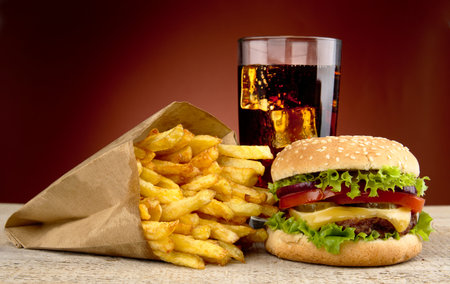 Cheeseburger with drink of cola, french fries on red spotligh