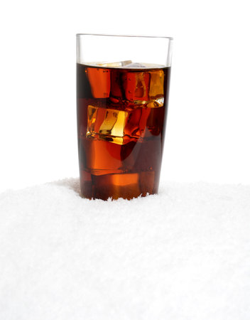 Glass of cola with ice cubes on snow on white background