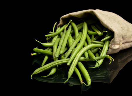 Stack of green beans in linen sack on black background