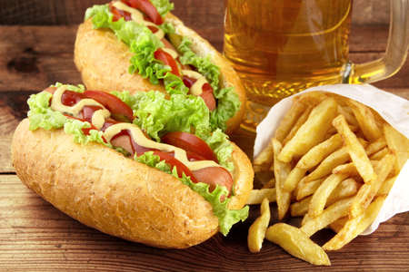 Hotdogs with glass of beer with french fries on wooden boardの写真素材