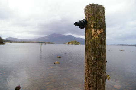 Lake background with a wooden pole in the front and a mountain at the back of the lakeの写真素材